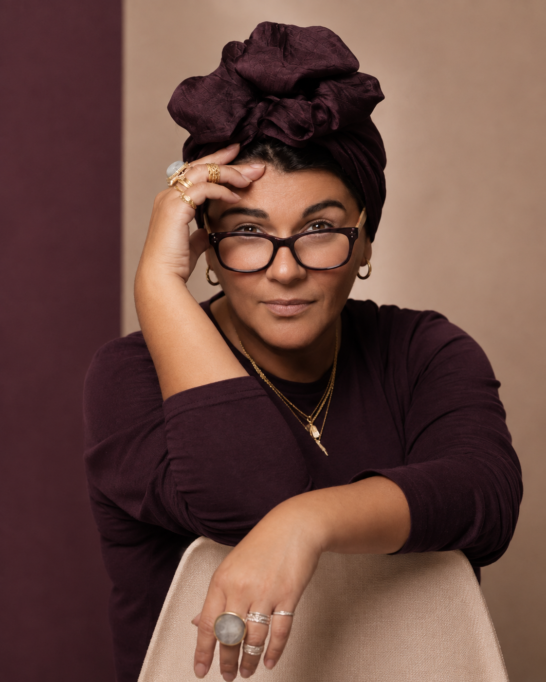 Portrait of Asil Attar in a plum headwrap and glasses against a plum and taupe backdrop