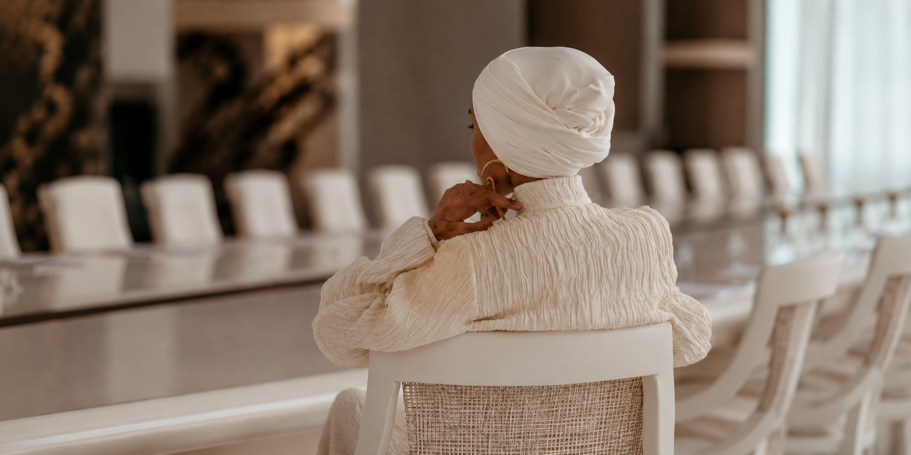 Woman seated alone at a long ivory boardroom table