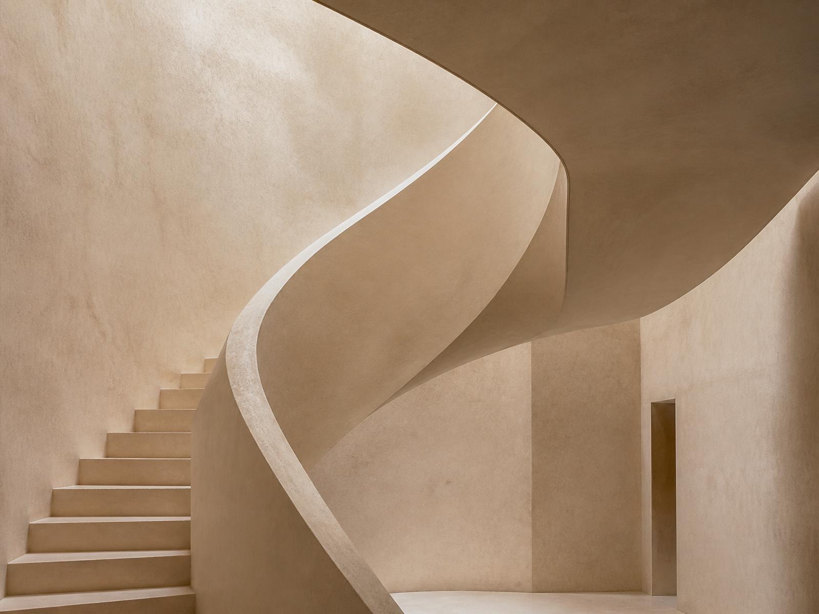 Sculptural plaster staircase curving through warm ivory light